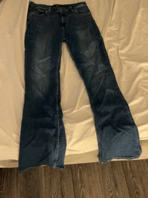 Blå bootcut jeans med utsvängda ben - Säljer ett par klassiska blå bootcut jeans med utsvängda ben och femficksmodell. Jeansen har normalhög midja och är tillverkade i denim med lätt tvättad look. Perfekta för dig som gillar retrostil och vill ha ett par snygga jeans med 2000-talsvibbar.