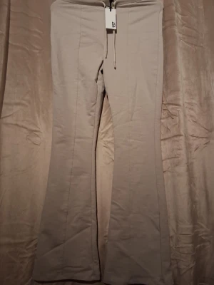 Beige mjukisbyxor från 157, bootcut - Säljer ett par beige mjukisbyxor från 157 med bootcut-modell och dragsko i midjan. Byxorna har en enkel och clean look, perfekta för chill dagar. Tillverkade i mjukt och stretchigt material för extra komfort.