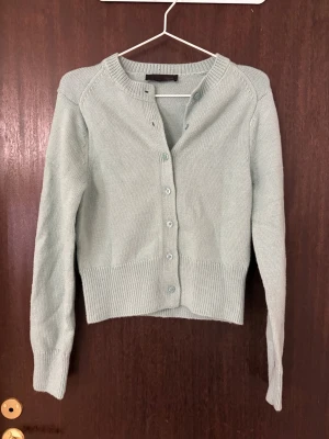 turkos ribbad kofta med knappar - Snygg turkos kofta med ribbade muddar och knappar framtill. Modellen är croppad och har lång ärm samt rund halsringning. Perfekt att slänga över en topp för en chill look. Aldrig använd.