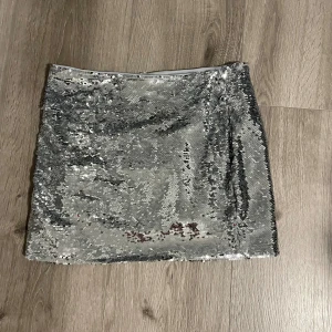 Silver paljettkjol från MNG - Säljer en glittrig silverfärgad kortkjol från MNG, täckt med paljetter som ger ett riktigt statement-utseende. Supersnygg att styla med en enkel topp eller kavaj. använd en gång 