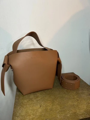 Acne Musubi väska brun  - Säljer nu denna bruna acne Musubi som mest stått och dammat ett bra tag, väldigt varsamt använd så i nytt skick! Inga defekter osv☺️ Axelband medföljer såklart. Kan gå ner i pris vid snabb affär! Postar snabbt😁