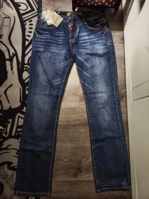 Blå raka jeans från Dsquared2 - Snygga blå jeans från Dsquared2 med raka ben och klassisk femficksdesign. Jeansen har slitningar och kontrastsömmar samt detaljerade bakfickor med broderi och patch. Tillverkade i denim med en cool tvättad look.