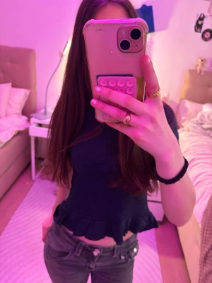 Mörkblå croppad topp med volang - Snygg mörkblå croppad topp med volangkant nedtill och korta ärmar. Perfekt för dig som gillar en enkel men ändå söt stil. Toppen har en figurnära passform och är tillverkad i ett mjukt material som känns skönt mot huden.