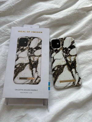 iDeal of Sweden Calcatta Golden Marble skal - Snyggt mobilskal från iDeal of Sweden i modellen Calcatta Golden Marble. Skalets design har vit bakgrund med svart och guldmarmorerat mönster. Passar till iPhone 11/XR. Tillverkat i hårdplast med gulddetalj på framsidan.