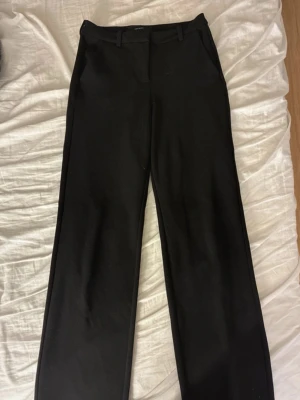 Svarta kostymbyxor från Vero Moda - Stilrena svarta kostymbyxor från Vero Moda med raka ben och klassisk passform. Byxorna har hällor för skärp och diskreta sidofickor. Perfekta för en clean och snygg look. Materialet är mjukt och följsamt.