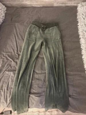 Gröna velourbyxor från Juicy Couture - Säljer ett par gröna mjukisbyxor från Juicy Couture i mjuk velour. Byxorna har bred resår i midjan med dragsko, stora fickor fram och broderad JC-logga på ena fickan. Perfekta för chill dagar och riktigt sköna att ha på sig.