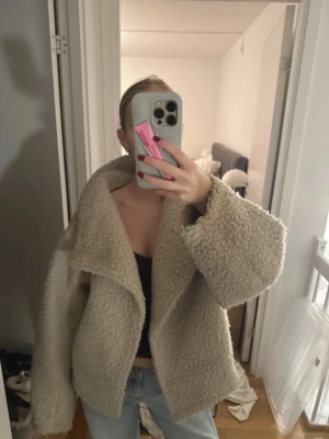 Beige oversized teddyjacka - Säljer en beige oversized teddyjacka med stora slag och bred passform. Jackan har en fluffig, mjuk yta och stängs framtill med knappar. Perfekt för att hålla sig varm och snygg under kyliga dagar.