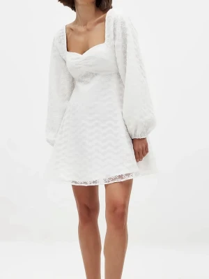 Studentklänning  - Supersöt vit kortklänning med puffiga långärmar och hjärtformad urringning. Klänningen har ett lager av spets med blommigt mönster och lätt volang i kjolen. Perfekt studentklänning!