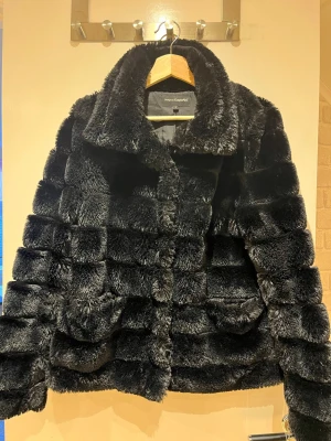 Svart pälsjacka  - Otroligt snygg och elegant svart pälsjacka från Kappahl. Jackan har en kortare modell och stängs med knappar. Jackan har dessutom två fickor, en på vardera sida. Perfekt att ha på sig både till fest och till vardags. OBS! Jackan är gjord på fuskpäls.