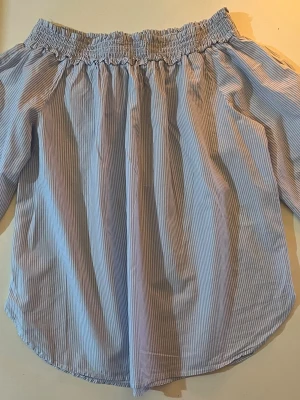 Blå offshoulder blus från H&M - Snygg blå- och vitrandig offshoulder blus från H&M med smockad resår upptill. Blusen har långa ärmar och är gjord i ett lätt, luftigt bomullstyg. Perfekt för en trendig och avslappnad look. Storlek 34 och CN 160/80A. (Har en vit sådan också, checka min profil). Använd några gånger, inga fläckar och ser helt ny ut.