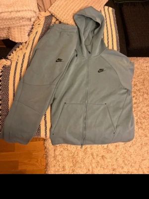 Ljusblå Nike mjukisbyxor - Snygga ljusblå mjukisbyxor från Nike med svarta loggor och dragsko i midjan. Byxorna har en modern passform med paneldetaljer och fickor på sidorna. Perfekta för en chill och sportig stil.