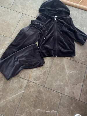 Brun velour loungewear-set - Mysigt brun loungewear-set i mjuk velour med dragkedja, huva och fickor på tröjan samt matchande byxor med resår i midjan. Perfekt för chill dagar hemma. Snyggt och bekvämt set som ger en avslappnad look.