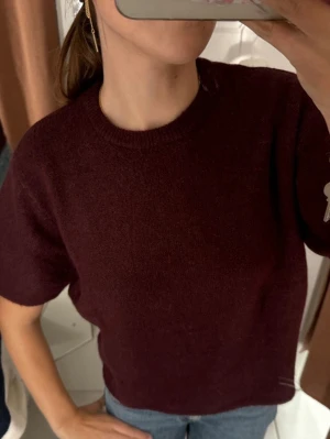 Mörkröd stickad t-shirt - Säljer en mörkröd stickad t-shirt med korta ärmar och rund halsringning. Tröjan har en enkel och stilren design, perfekt att matcha med jeans eller kjol. Använt 4 gånger💕 Säljer för att blev trött på färgen🤍