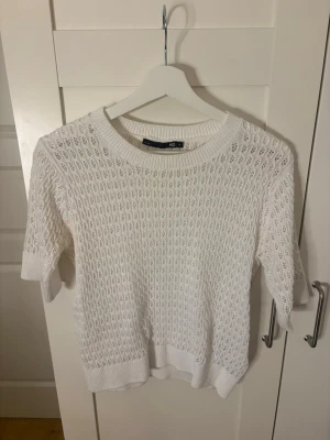 Stickad topp - Säljer en vit stickad topp från 157 med korta ärmar och rund hals. Tröjan har ett luftigt hålmönster och ribbade muddar vid ärmslut och nederkant. Knappt använd!