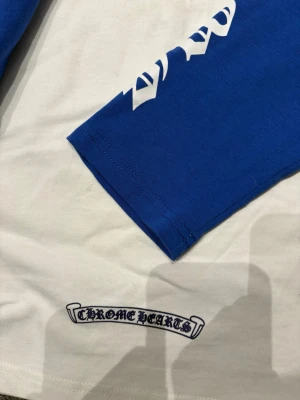 Blå långärmad topp från Chrome Hearts - Säljer en blå långärmad topp från Chrome Hearts med vit logga tryckt på ärmen och en mindre logga på framsidan. Toppen har en klassisk passform och är gjord i mjuk bomull. Perfekt för dig som gillar streetwear och vill sticka ut.
