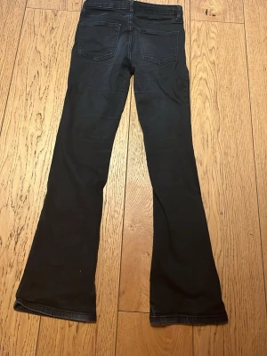 Svarta bootcut jeans - Säljer ett par svarta bootcut jeans med klassisk femficksdesign och utsvängda ben. Jeansen har normalhög midja och är sydda i ett stretchigt denimtyg som sitter snyggt. Perfekta för dig som gillar en tidlös och trendig look.