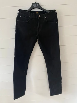 Svarta skinny jeans från Lee - Säljer ett par svarta jeans från Lee med klassisk femficksmodell och knappgylf. Jeansen har en smal passform och är tillverkade i stretchigt denimtyg för extra komfort. Perfekta för dig som gillar en stilren och enkel look. Stl.30*32