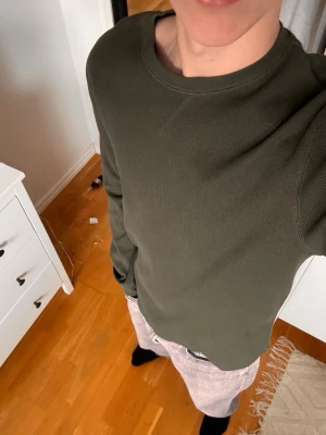 Mörkgrön långärmad tröja från Kappahl - Säljer en stilren mörkgrön långärmad tröja i mjukt material. Tröjan har rund halsringning och en enkel, klassisk design utan tryck eller mönster. Perfekt för dig som gillar en clean och avslappnad look. Storlek S
