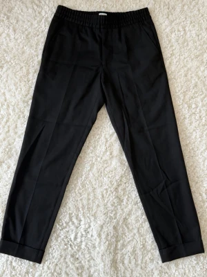 Avslappnade kostymbyxor från Filippa K, strl 44, svart - Avslappnade och eleganta kostymbyxor från Filippa K. Använda men i fint skick. •Storlek 44 •Dragkedjegylf/snörad resårmidja •pressveck •Två snedställda framfickor samt två bakfickor •Tillverkade i en ull- och polyesterblandning 💸Nypris ca 1700kr