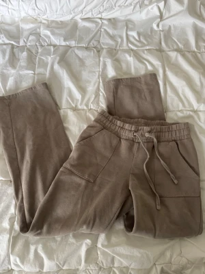 Beige mjukisbyxor med dragsko - Säljer ett par beige mjukisbyxor med bred resår i midjan och justerbar dragsko. Byxorna har raka ben och stora fickor framtill. Fickor baktill.  Bandet i midjan är lite slitet, samt små små fläckar nedtill på ena benet ( kan gå bort men är inte säker)  storlek S från lager157. 