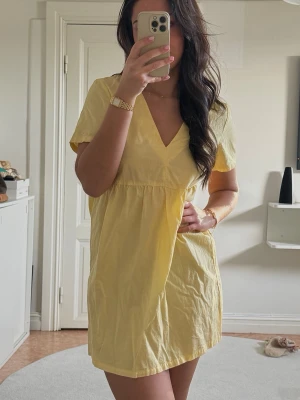 Gul kort klänning med v-ringning - Söt gul kortklänning med v-ringning och korta ärmar. Klänningen har en avslappnad passform och är perfekt för varma dagar. Tillverkad i ett lätt och bekvämt material som känns skönt mot huden.