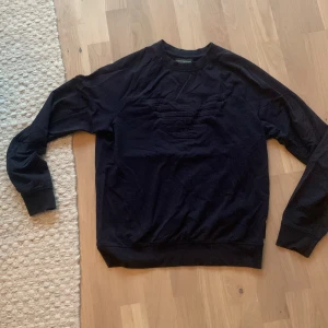  sweatshirt från Emporio Armani -  sweatshirt från Emporio Armani med stort, diskret broderat logotypmönster på bröstet. Tröjan har rund hals, långa ärmar och ribbade muddar. Tillverkad i mjuk bomull för en skön och stilren look.