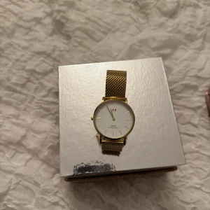 Guldig klocka Lorenzo Milano meshband - Stilren klocka från Lorenzo Milano med vitt urtavla och guldig mesh-länk. Klockan har minimalistisk design med tunna index och italiensk flagga på urtavlan. Perfekt accessoar för dig som gillar klassisk och elegant stil.