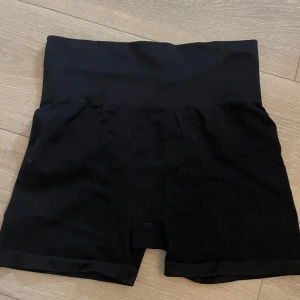 Svarta sportshorts från H&M - Svarta, ribbade sportshorts från H&M med hög midja och stretchigt material. Perfekta för träning eller chill dagar. Snygg, enkel design med diskreta vertikala ränder och bekväm passform.