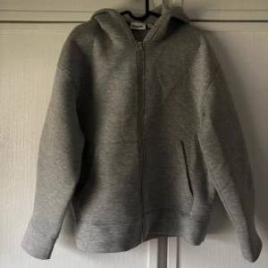 Grå hoodie med dragkedja från Kappahl - Säljer en grå hoodie från Kappahl i storlek S. Tröjan har huva, hel dragkedja framtill och två fickor. Nypris 499. Tjockt material. 