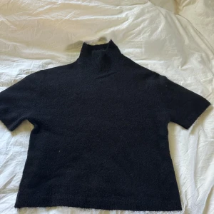 Svart polotröja i ullblandning Gina Tricot - Svart polotröja från Gina Tricot i mjuk ullblandning. Tröjan har korta ärmar och hög krage, perfekt för lager-på-lager. Enkel och stilren design som funkar till allt. Snygg att matcha med jeans eller kjol.