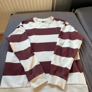 Randig sweatshirt från Lager 157, stl S - Säljer en oversized sweatshirt från 157 i storlek S. Tröjan har breda vinröda och vita ränder, rund hals och långa ärmar. Perfekt för dig som gillar en avslappnad och trendig stil. Materialet är mjukt och skönt, troligtvis bomull.
