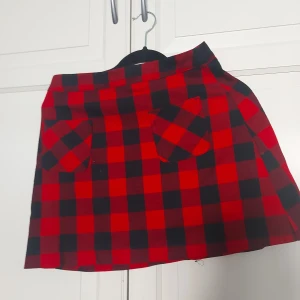 Rutig röd minikjol från H&M Divided - ⚠️ Skriv till mig innan köp!⚠️Snygg röd och svart rutig kortkjol från H&M Divided med två fickor framtill och dragkedja bak. Kjolen har klassiskt rutmönster och är gjord i bomullstyg, perfekt för en cool och avslappnad stil. 