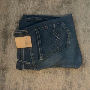 Replay Hyperflex jeans i mörkblå denim - Säljer ett par Replay Hyperflex jeans i mörkblå denim med klassisk femficksdesign och snygga kontrastsömmar på bakfickan. Jeansen har en rak passform och är tillverkade i stretchigt jeansmaterial för extra komfort. Perfekta för dig som gillar stilrena och bekväma jeans.