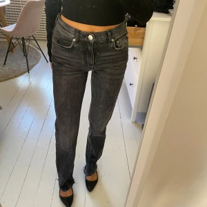 Nicki Studios x Gina Tricot svarta jeans - Snygga svarta jeans från Nicki Studios x Gina Tricot med hög midja och raka ben. Jeansen har slitna detaljer vid fickorna och råa benslut för en cool vibe. Klassisk femficksmodell i tvättad svart denim med dragkedja och knapp.