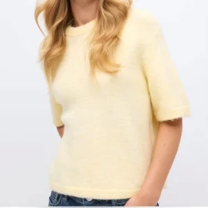 Ljusgul stickad tröja med kort ärm från gina - Superfin ljusgul stickad tröja med korta ärmar och rund hals. Mjuk och fluffig känsla, perfekt till jeans eller kjol. Enkel och stilren design som ger en fräsch look.