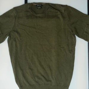 Olivgrön stickad tröja från Massimo dutti - En stilren olivgrön stickad tröja från Massimo dutti med rund halsringning och långa ärmar. Tröjan har en klassisk passform och ribbade muddar vid ärmslut och nederkant. Perfekt för lager-på-lager under kyliga dagar.