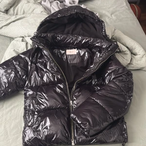 Svart pufferjacka ifrån Nelly med luva ❤️ - Säljer en svart, glansig pufferjacka från Nelly i storlek S. Jackan har huva, tvåvägsdragkedja och praktiska fickor med tryckknappar. Perfekt för kalla dagar och ger en cool vibe till din outfit. Inga skador alls!!!