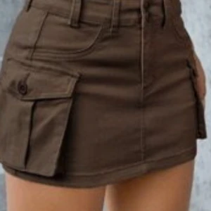 Brun cargo minikjol med fickor - Säljer en brun kort cargo-kjol med stora sidofickor och bälteshällor. Kjolen har en klassisk jeanslook med knapp och dragkedja framtill. Perfekt för dig som gillar utility-stil och vill ha en cool och praktisk kjol i garderoben. Säljer då jag inte använder den så mycket