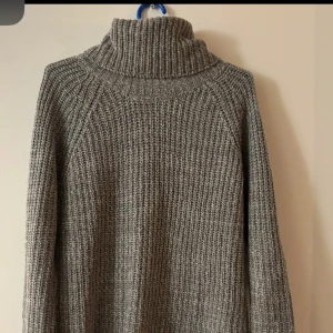 Grå stickad polotröja från X&CIRCLE - Mysig grå stickad polotröja från X&CIRCLE i storlek S. Tröjan har en hög polokrage, långärmad design och grovstickad struktur som ger en chill och avslappnad vibe. Perfekt för lager på lager under kyliga dagar.