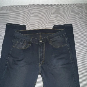 Levi's 512 mörkblå jeans  - Säljer ett par Levi's 512 jeans i mörkblå tvätt med klassiska gula sömmar. Modellen har smal passform och raka ben, fem fickor och Levi's ikoniska läderpatch bak. Perfekta för dig som gillar stilrena och tidlösa jeans.
