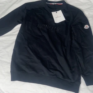 Svart sweatshirt från Moncler - Säljer en svart sweatshirt från Moncler med broderad logga på bröstet och klassisk Moncler-patch på ärmen. Tröjan har rund halsringning och långa ärmar. Perfekt för dig som gillar stilrena och exklusiva plagg.