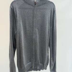 Grå stickad kofta med dragkedja - En stilren grå stickad kofta med hel dragkedja framtill och ribbad krage. Perfekt för lager-på-lager och enkel att matcha med andra plagg. Långärmad och med mjuk känsla, passar dig som gillar en clean och enkel look.
