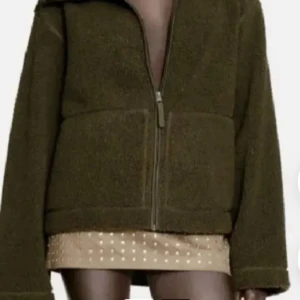 Olivgrön teddyjacka med dragkedja - Mysig olivgrön teddyjacka med hög krage och hel dragkedja framtill. Jackan har en loose passform och är tillverkad i mjukt fleece-material som ger en avslappnad och trendig look. Perfekt för kyliga dagar när du vill vara både bekväm och snygg.