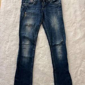 Diesel Matic low waist jeans blå W25 L32 - Snygga blå Diesel Matic jeans low med slitningar och trasiga detaljer på benen. Jeansen har klassisk femficksdesign, stretchigt material och en smal passform. Perfekta för dig som gillar en lite ruffare streetstil.