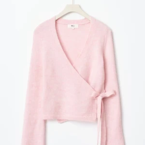 Ljusrosa omlottkofta från Gina Tricot - Superfin ljusrosa stickad kofta från Gina Tricot med omlottmodell och knyt i sidan. Tröjan har lång ärm och ribbade muddar vid ärmslut och nederkant.