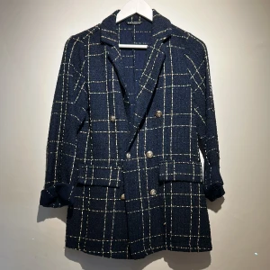 Mörkblå rutig kavaj från SHEIN - Stilren mörkblå kavaj från SHEIN med vitt rutmönster och snygga silvriga knappar. Jackan har dubbelknäppning, klassisk krage och två fickor framtill. Materialet är strukturerat och ger en lyxig känsla. Perfekt för dig som vill sticka ut med en trendig look. 