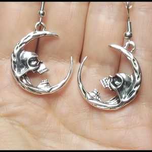  Helt nya Silvriga örhängen med dödskalle och måne -  Helt nya Unika silvriga örhängen i form av en halvmåne med detaljerad dödskalle i mitten. Cool design som sticker ut och passar perfekt för dig som gillar alternativ stil. Hängande modell med metallkrok för enkel användning.