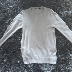 Ljusgrå stickad tröja J.Lindeberg - Snygg ljusgrå stickad tröja från J.Lindeberg i storlek S. Tröjan har rund halsringning, diskret logga på bröstet och är tillverkad i mjuk merinoull. Perfekt för lager-på-lager och passar till allt. Klassisk och stilren design med långa ärmar.