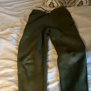 Olivgröna mjukisbyxor från Nike S - Säljer ett par olivgröna mjukisbyxor från Nike i storlek S. Byxorna har dragsko i midjan, diskret Nike-logga på benet och praktiska fickor med dragkedja. Perfekta för chill eller träning, tillverkade i mjukt material för maximal komfort.