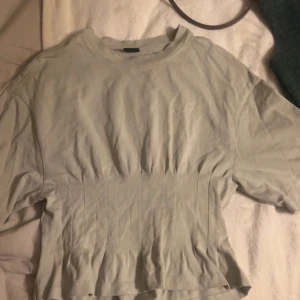 Beige croppad topp med sömdetaljer - Säljer en beige croppad topp med korta ärmar och rund halsringning. Toppen har markerade vertikala sömmar som ger en snygg form och lite ribbad känsla. Perfekt för dig som gillar en enkel men trendig stil.